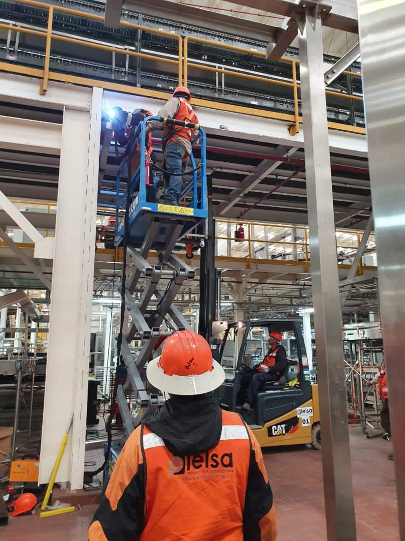 Plataforma de tijera eléctrica junto a montacargas en planta
